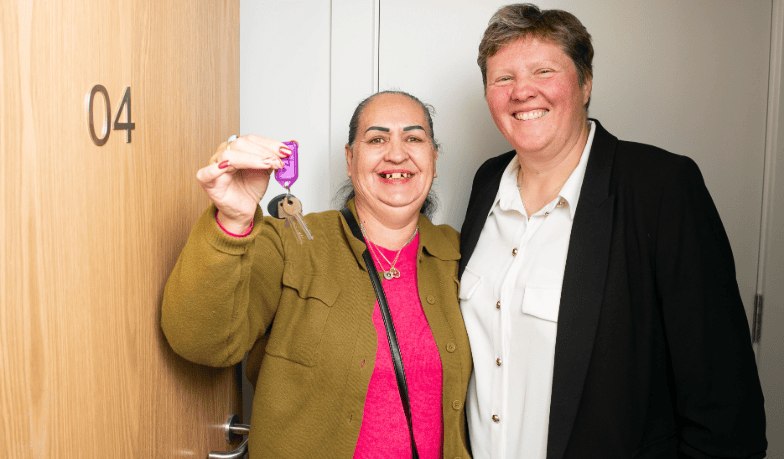 Two women standing at a door. One of the women is holding keys up to the camera.